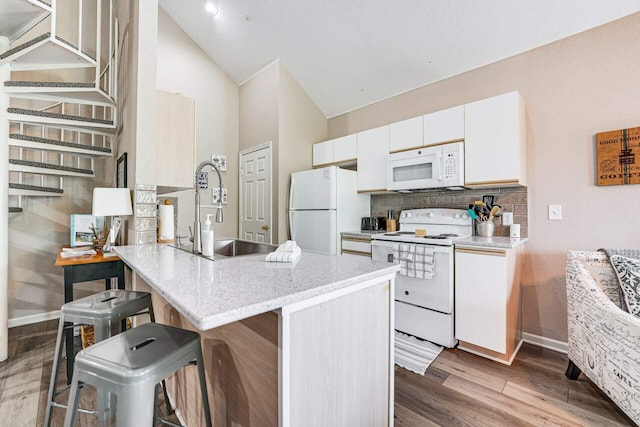 kitchen featuring lofted ceiling, sink, a breakfast bar area, white appliances, and white cabinets