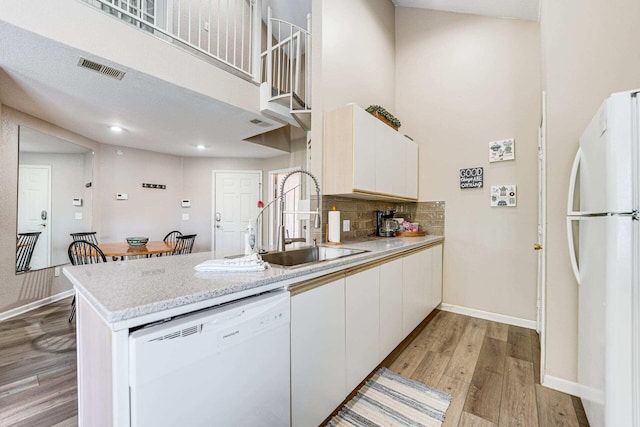 kitchen featuring a towering ceiling, sink, light wood-type flooring, white cabinets, and white appliances