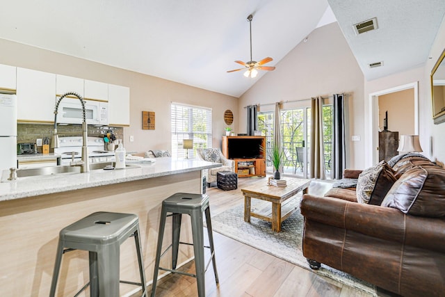 living room with ceiling fan, high vaulted ceiling, and light hardwood / wood-style floors