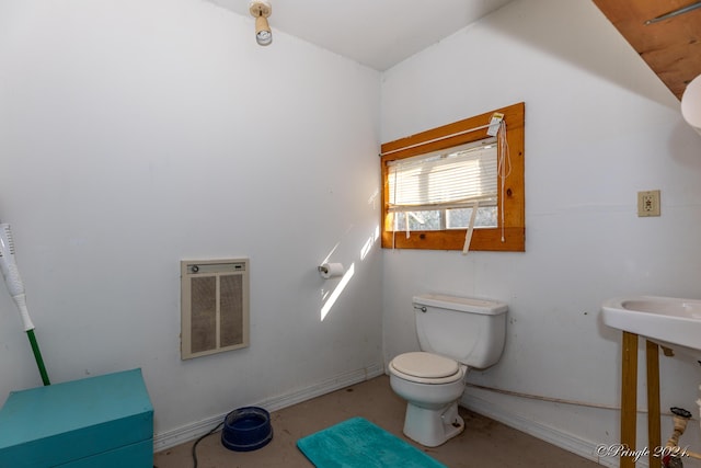 bathroom with heating unit, concrete floors, and toilet