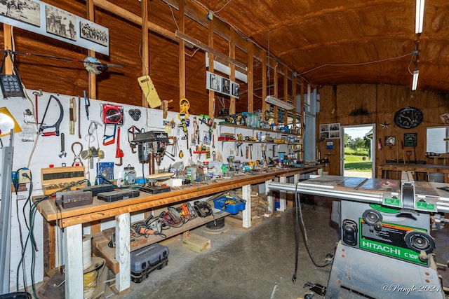 miscellaneous room featuring lofted ceiling, wooden walls, a workshop area, and concrete floors