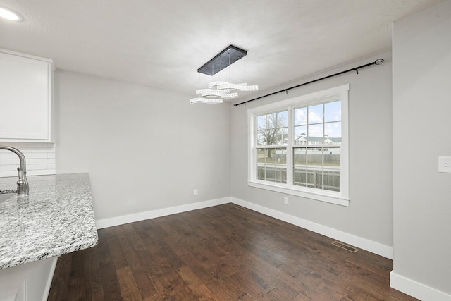 unfurnished dining area featuring dark hardwood / wood-style floors, sink, and a notable chandelier