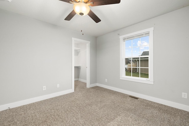 unfurnished bedroom with carpet, a spacious closet, ceiling fan, and a closet