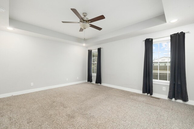 carpeted empty room with ceiling fan and a tray ceiling