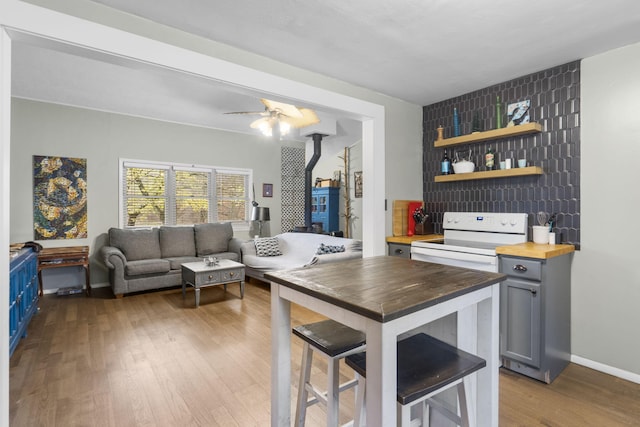 kitchen featuring a breakfast bar area, butcher block counters, gray cabinetry, light wood-type flooring, and a wood stove