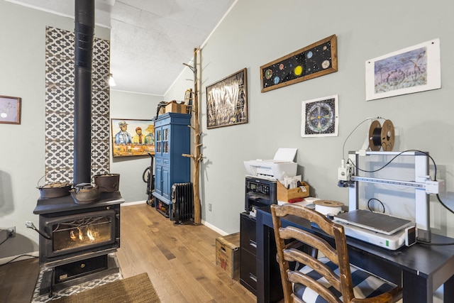 office space featuring lofted ceiling, light hardwood / wood-style flooring, ornamental molding, and a wood stove