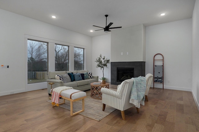 living room featuring ceiling fan, a tiled fireplace, and light hardwood / wood-style flooring