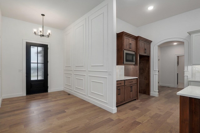 kitchen featuring pendant lighting, built in microwave, hardwood / wood-style flooring, a notable chandelier, and dark brown cabinets