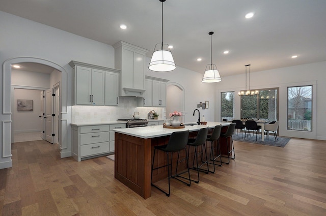 kitchen with a large island, light hardwood / wood-style flooring, stainless steel gas stove, hanging light fixtures, and backsplash