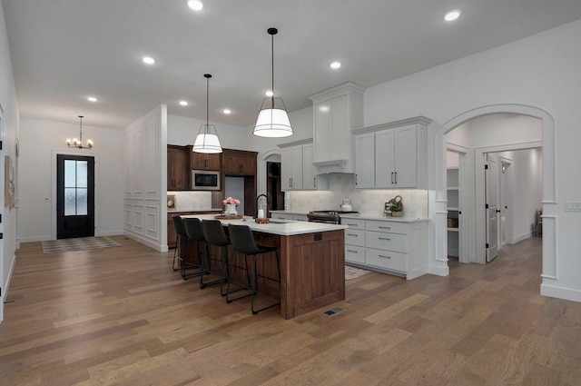 kitchen with sink, appliances with stainless steel finishes, white cabinets, a kitchen island with sink, and backsplash