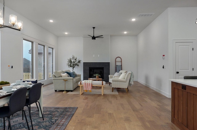 living room with ceiling fan with notable chandelier, light hardwood / wood-style floors, and a large fireplace