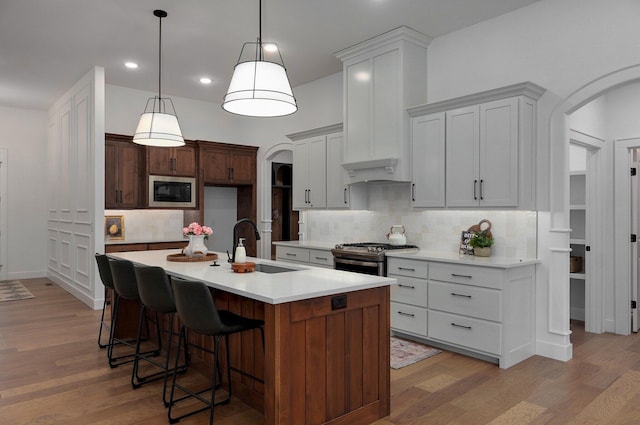 kitchen featuring built in microwave, sink, stainless steel gas stove, light hardwood / wood-style flooring, and an island with sink