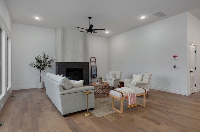 living room with a large fireplace, ceiling fan, and light wood-type flooring