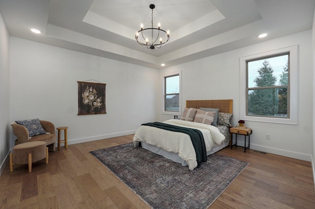 bedroom featuring a raised ceiling, wood-type flooring, and multiple windows