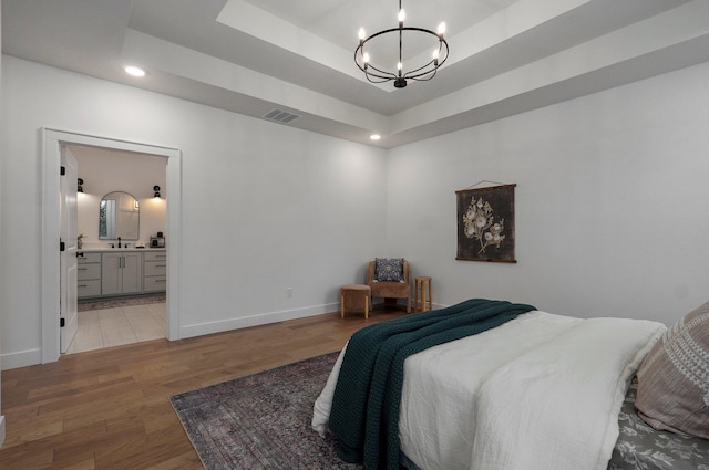 bedroom with ensuite bathroom, sink, a raised ceiling, a notable chandelier, and hardwood / wood-style flooring