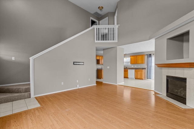 unfurnished living room with a tiled fireplace, a high ceiling, and light wood-type flooring