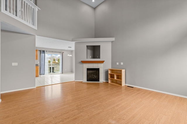 unfurnished living room featuring a fireplace, light hardwood / wood-style floors, and a high ceiling