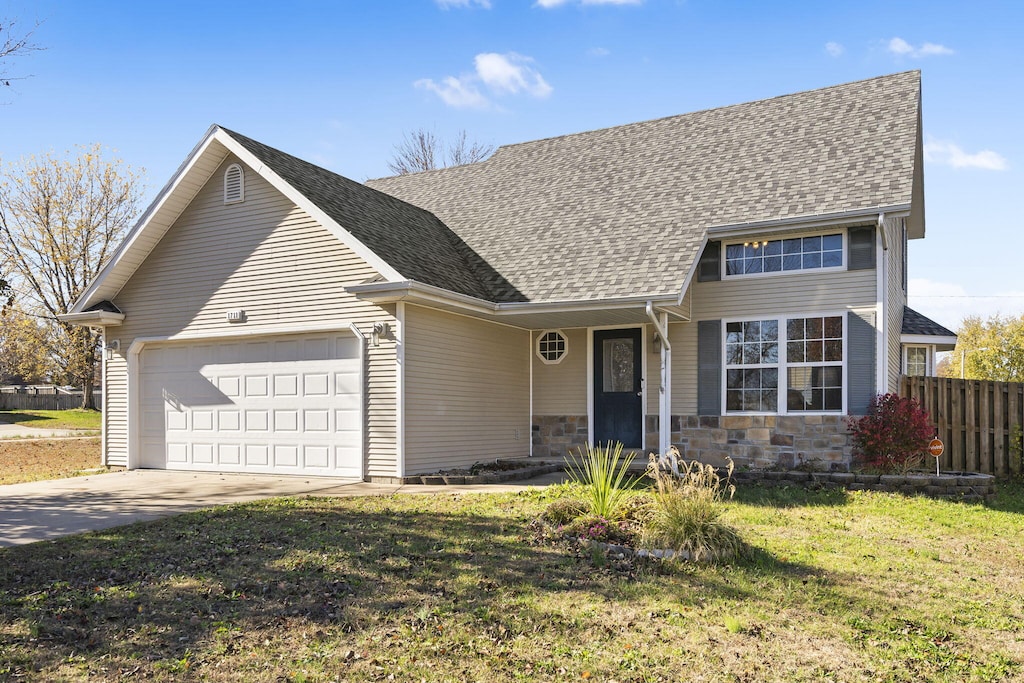 traditional-style home featuring concrete driveway, a front lawn, an attached garage, fence, and roof with shingles