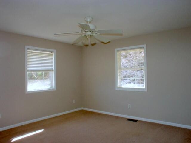 empty room featuring carpet floors, a ceiling fan, visible vents, and baseboards