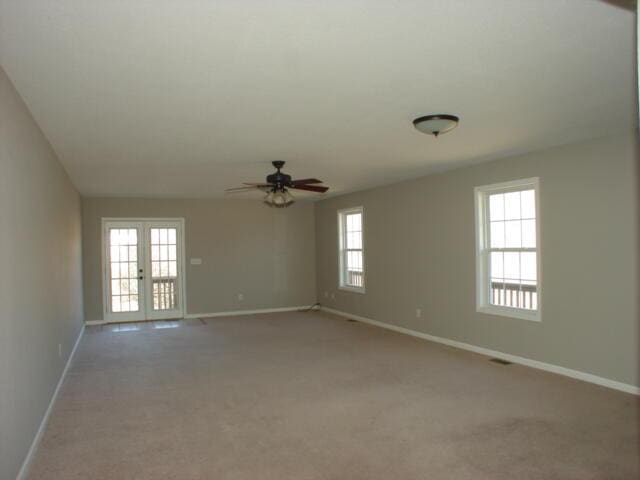 spare room featuring french doors, light colored carpet, plenty of natural light, and baseboards