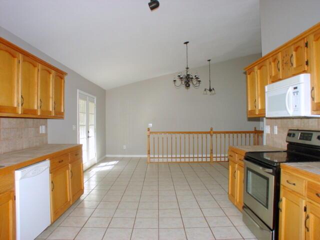 kitchen with white appliances, light tile patterned floors, tile counters, lofted ceiling, and hanging light fixtures