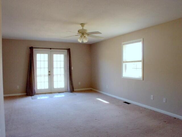 spare room with light carpet, baseboards, visible vents, a ceiling fan, and french doors