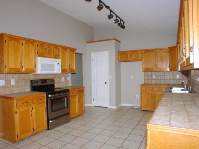 kitchen featuring light tile patterned floors, white microwave, vaulted ceiling, stainless steel range with electric cooktop, and a sink