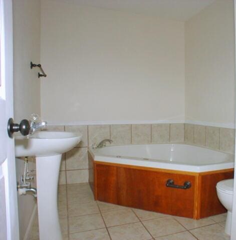 bathroom featuring wainscoting, toilet, tile patterned floors, a garden tub, and tile walls