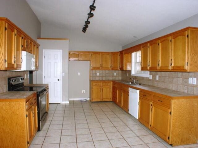 kitchen with white appliances, light tile patterned floors, brown cabinetry, lofted ceiling, and light countertops