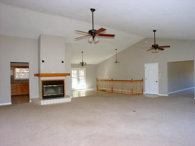 unfurnished living room with a glass covered fireplace, light colored carpet, ceiling fan, french doors, and high vaulted ceiling