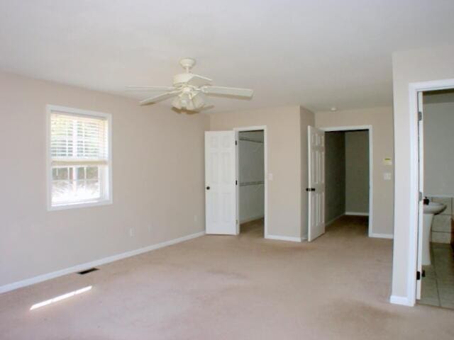 unfurnished bedroom featuring visible vents, baseboards, light colored carpet, ceiling fan, and a spacious closet