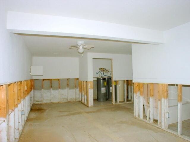 unfurnished room with a wainscoted wall, water heater, a ceiling fan, wooden walls, and concrete floors