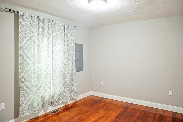 unfurnished room with hardwood / wood-style flooring, electric panel, and a textured ceiling