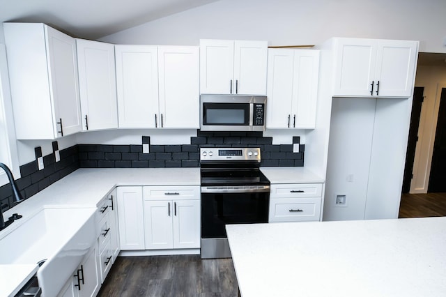 kitchen featuring dark wood-type flooring, white cabinetry, vaulted ceiling, appliances with stainless steel finishes, and backsplash