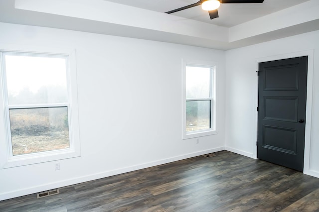 empty room with ceiling fan, dark hardwood / wood-style flooring, and a raised ceiling