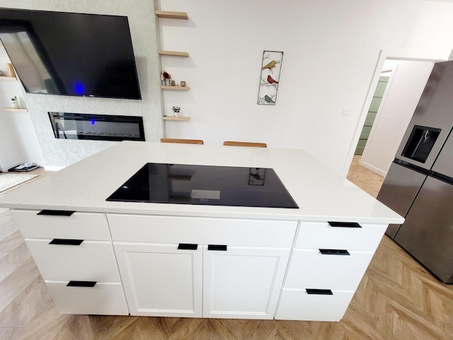 kitchen featuring stainless steel fridge, light parquet floors, light stone countertops, white cabinets, and black electric cooktop