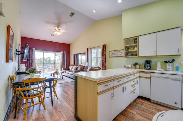 kitchen featuring light countertops, lofted ceiling, a peninsula, wood finished floors, and white dishwasher