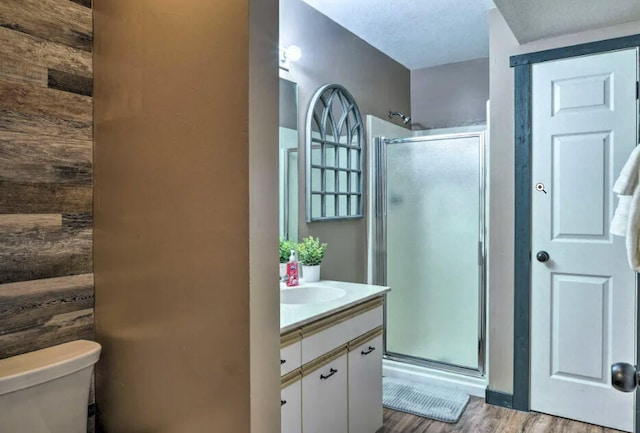 bathroom featuring vanity, toilet, wood finished floors, and a stall shower