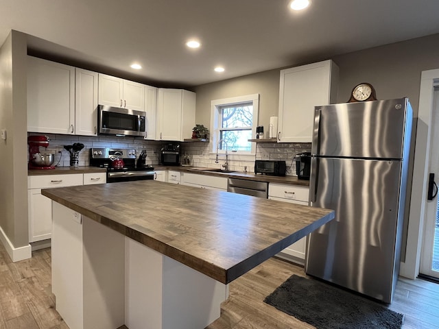 kitchen with wooden counters, white cabinetry, stainless steel appliances, a center island, and light wood-type flooring