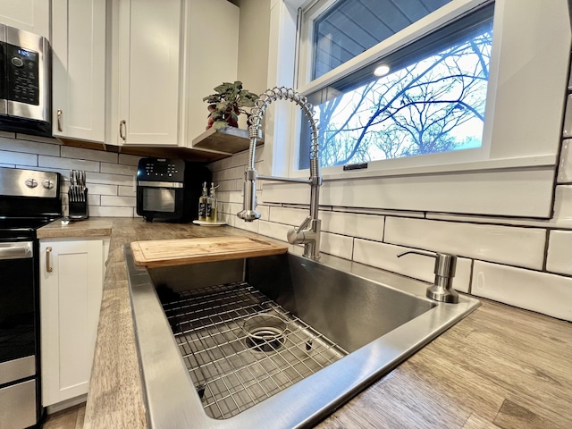 kitchen featuring appliances with stainless steel finishes, white cabinetry, sink, backsplash, and wooden counters