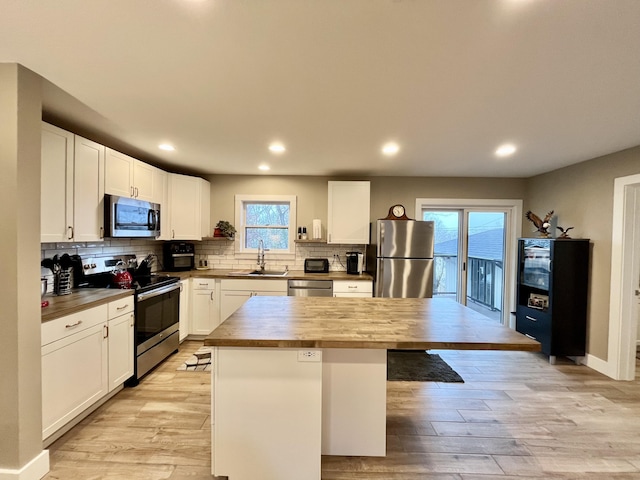 kitchen with wood counters, sink, appliances with stainless steel finishes, a kitchen island, and white cabinets