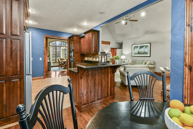 kitchen featuring ceiling fan, lofted ceiling with beams, kitchen peninsula, oven, and light wood-type flooring