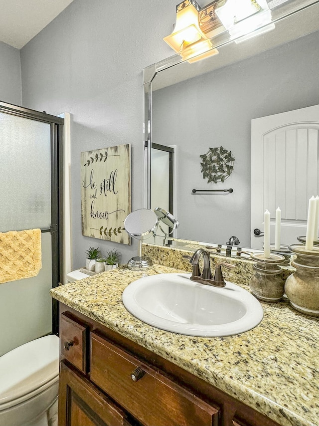 bathroom with vanity, a shower with shower door, and toilet