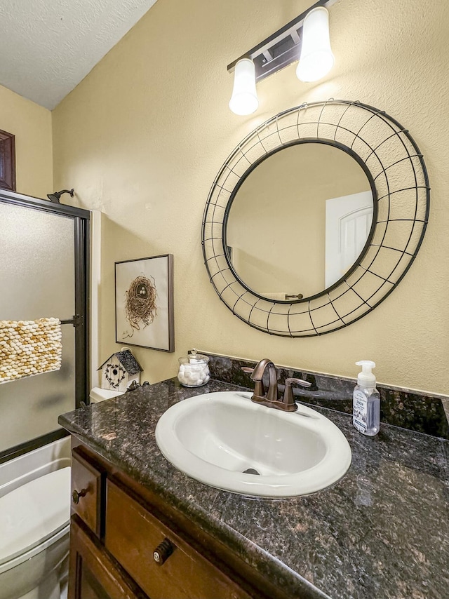 bathroom featuring vanity, a shower with shower door, toilet, and a textured ceiling