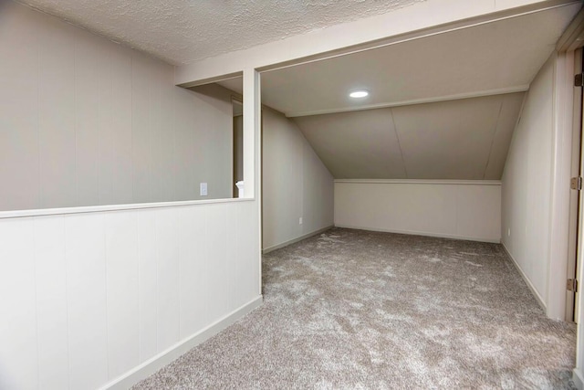 additional living space featuring vaulted ceiling, light carpet, and a textured ceiling