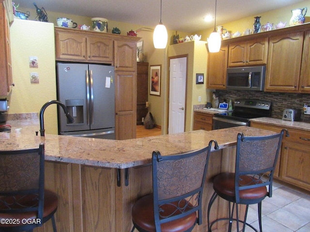 kitchen with a breakfast bar, appliances with stainless steel finishes, light stone counters, decorative backsplash, and kitchen peninsula