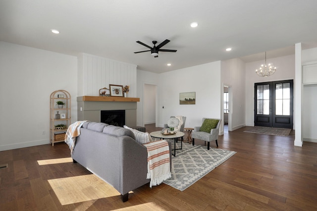 living room with dark wood-type flooring, a large fireplace, ceiling fan with notable chandelier, and french doors