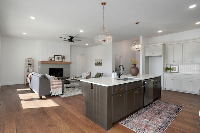 kitchen with dark hardwood / wood-style floors, pendant lighting, dishwasher, sink, and a center island with sink