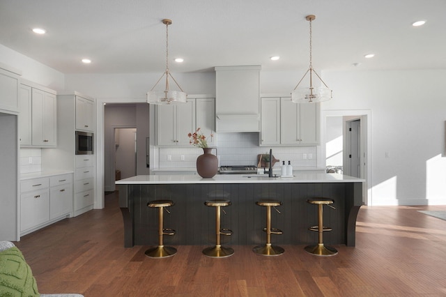 kitchen with backsplash, dark hardwood / wood-style floors, a spacious island, built in microwave, and decorative light fixtures