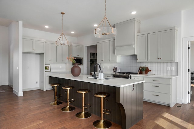 kitchen featuring sink, stainless steel gas stove, an island with sink, pendant lighting, and decorative backsplash